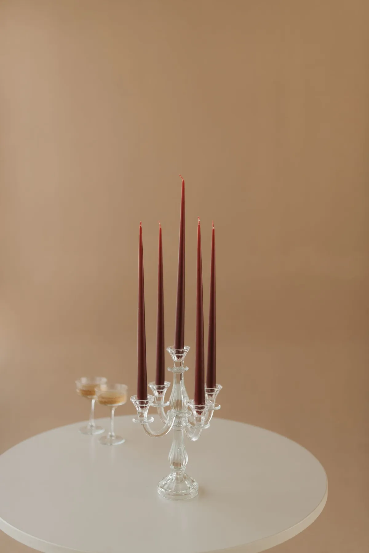 Velas altas cor de vinho num castiçal de vidro sobre mesa clara, com fundo bege